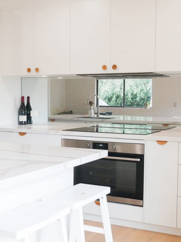 Mirrored Splashback Mirrored splashback in white kitchen with wooded handles