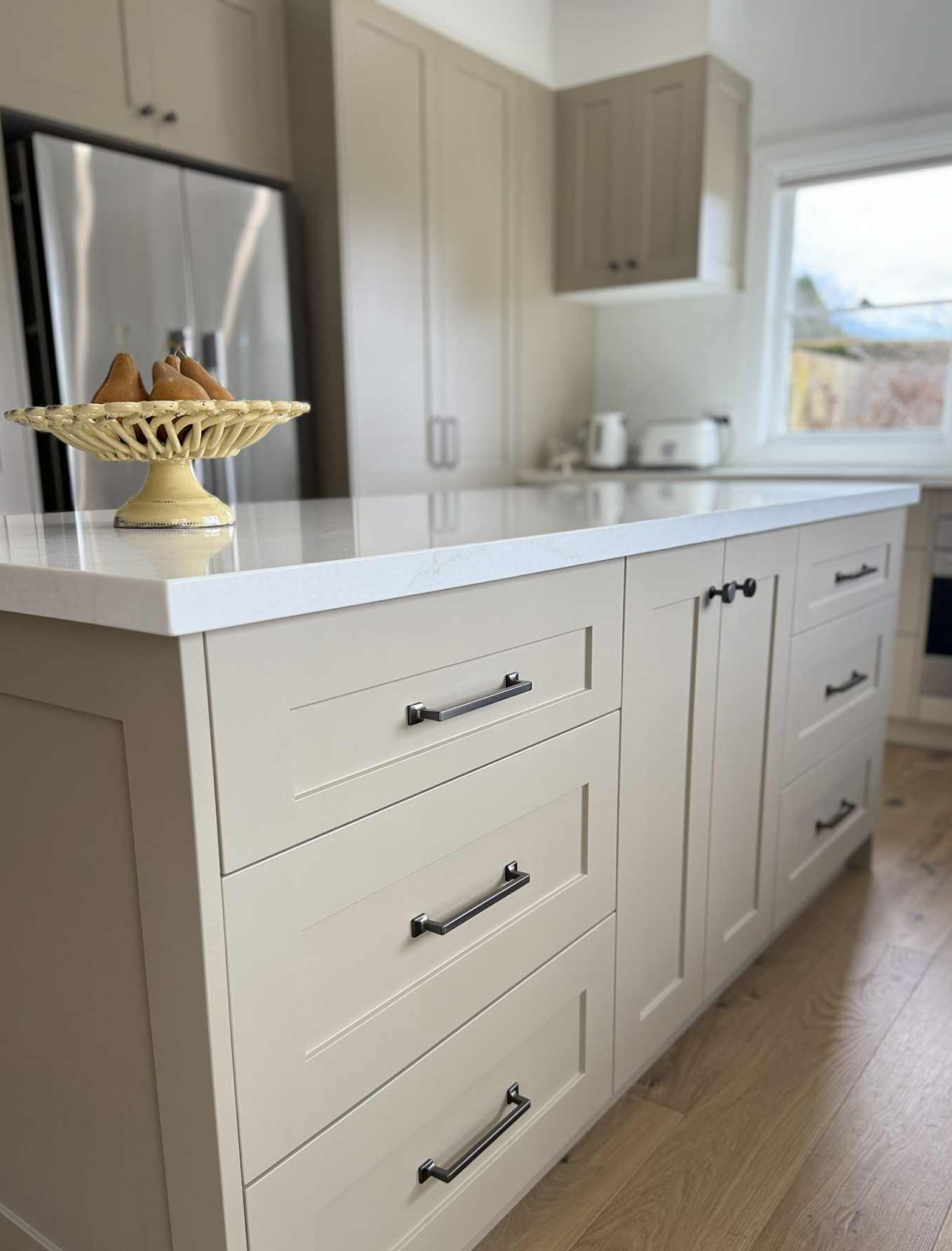 Hamptons-style cabinetry painted in Resene Triple Bison Hide. A warm neutral tone that creates a calm and welcoming atmosphere. The design is elevated with a YDL Stone Vene Rose benchtop and matching splashback, complemented by sleek stainless steel appliances and inviting seating.